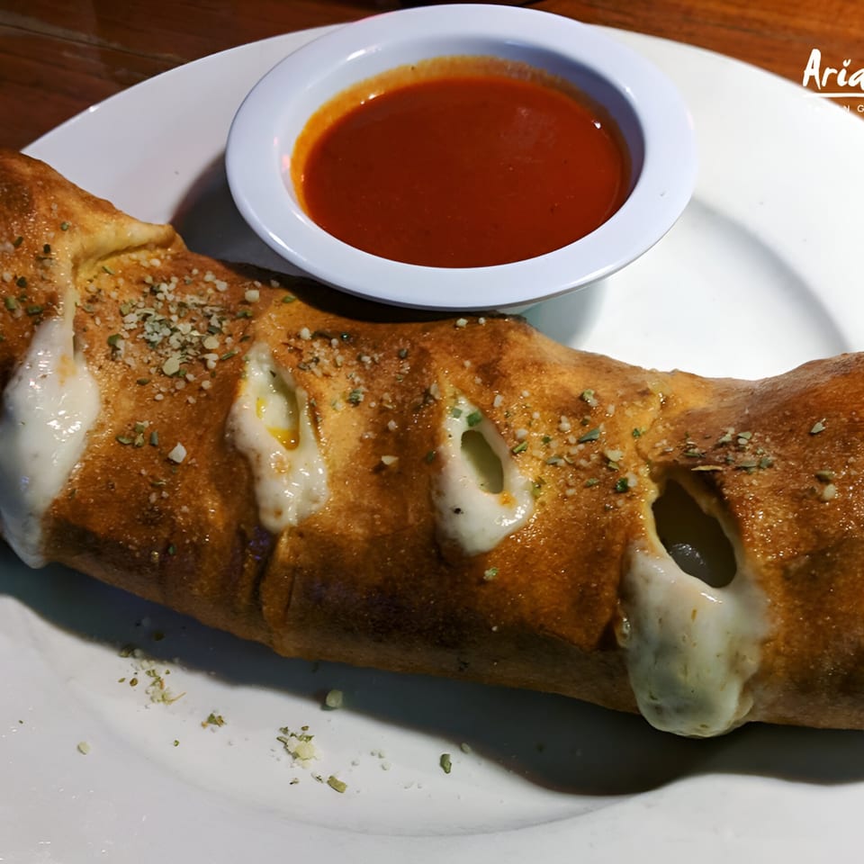 A golden-brown calzone with melted cheese oozing out, served with a side of red marinara sauce.