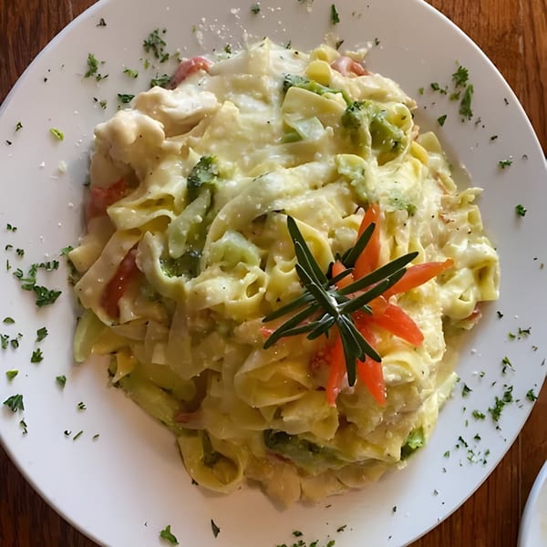 Creamy fettuccine pasta with broccoli, tomatoes, and herbs on a white plate at Arianna's Italian Grill.