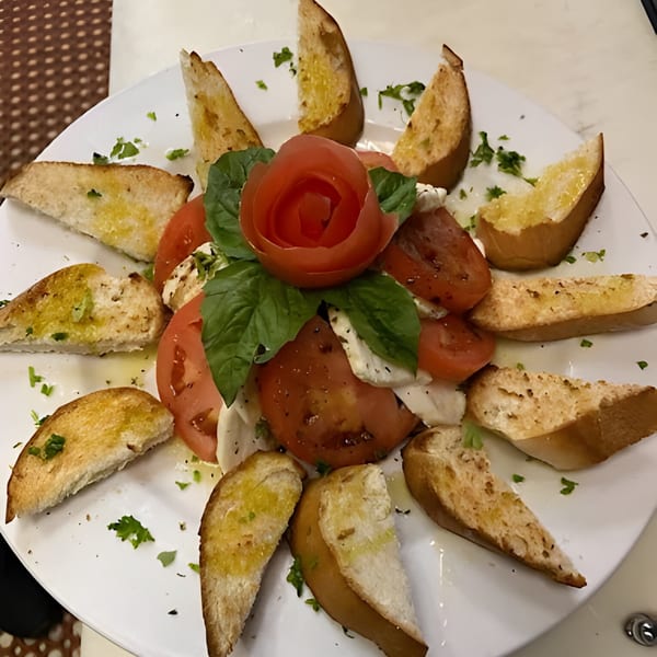 Caprese salad with tomato, mozzarella, basil, and garlic bread on a white plate.