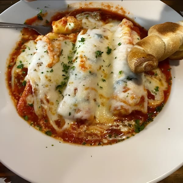 Baked ziti or lasagna with melted cheese, red sauce, and a breadstick on a white plate.