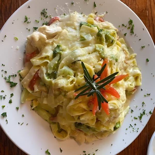Creamy pasta dish with broccoli, tomatoes, and herbs on a white plate at Arianna's Italian Grill.