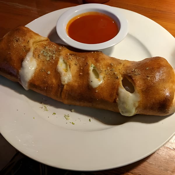 A golden-brown calzone with melted cheese oozing out, served with a side of red marinara sauce.