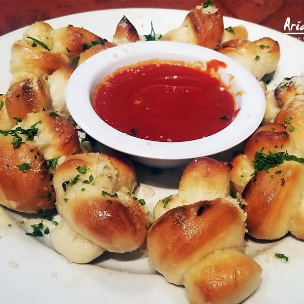 Garlic knots from Arianna's Italian Grill, garnished with parsley and served with marinara sauce.