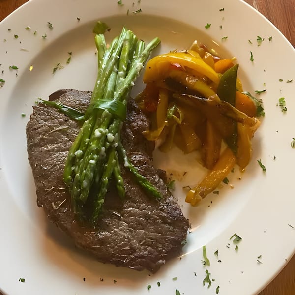 Grilled steak with a bundle of asparagus and sautéed yellow bell peppers on a white plate.